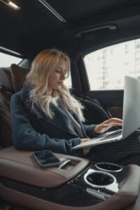 Femme d'affaires travaillant à distance sur un ordinateur portable, assise à l'arrière d'une voiture de luxe. Élégante, moderne et concentrée.